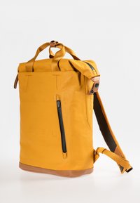 Zaino giallo a sacca realizzato in materiale resistente, dotato di tasca laterale con zip, fondo rinforzato e spallacci regolabili con rivestimento in rete.