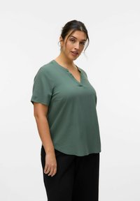 Top de manga corta y escote en pico en verde apagado, confeccionado en una tela suave con un corte holgado, que presenta detalles de costura sutiles.