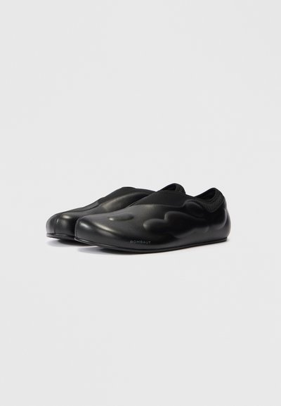 Scarpe slip-on nere realizzate in materiale liscio con punta arrotondata e dettaglio della superficie ondulata testurizzata. Il nome del marchio "ROMBAUT" è visibile.