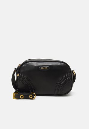 Borsa a tracolla nera in pelle con accenti curvi, hardware dorato, chiusura con zip e una tracolla regolabile con ritagli circolari.