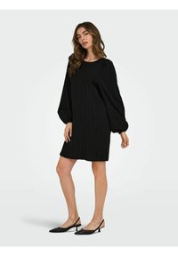 Black striped dress with long, puffy sleeves and a loose fit, knee-length; paired with black slingback heels featuring a pointed toe.