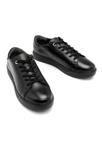 Sneaker in pelle nera con chiusura a lacci, punta rotonda e superficie liscia. Presenta occhielli dorati e una suola in gomma texturizzata.