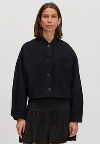 Zwarte cropped jas van zachte stof, met een staande kraag, frontsluiting met knopen en een enkele borstzak. Gladde textuur.