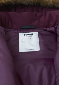 Vnitřek vínově červené prošívané bundy obsahující štítek s péčí, značkou "Reima", velikostí "104 / 4T" a zprávou o předání předmětu dál.