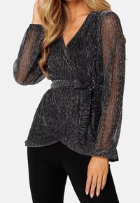 Blouse portefeuille noire avec fil métallique, col en V profond, manches longues transparentes, et ceinture à nouer. Design drapé avec ourlet évasé.