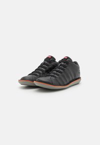Scarpe sportive nere con tomaie testurizzate, accentuate di arancione lungo le suole, e design con lacci. Punta arrotondata e suola in gomma.