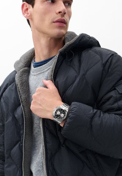 Geacă matlasată neagră cu căptușeală gri din fleece, pulover gri și ceas din oțel inoxidabil cu cadran negru și funcții cronograf.