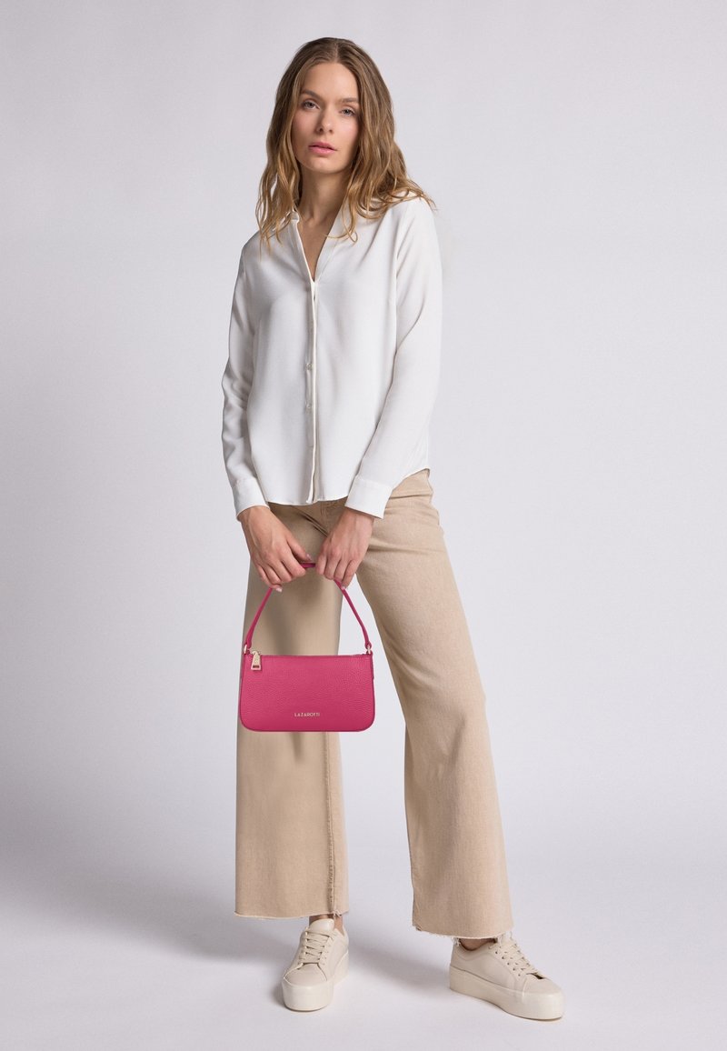 Camisa blanca de manga larga y botón, pantalones beige de pierna ancha y zapatillas de plataforma color crema. Sosteniendo un bolso texturizado de color rosa brillante con logo.