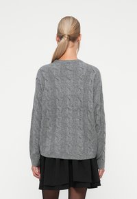 Siva pletena jopica z ohlapnim krojem, z žametnim ovratnikom in robom. Na hrbtni strani je teksturiran vzorec, v kombinaciji s plastenim črnim krilom.