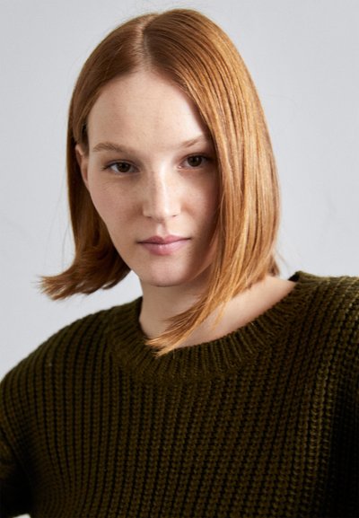 Gestrickter Pullover in dunklem Grün mit rundem Ausschnitt und Rippstruktur. Modell mit schulterlangem, glattem Haar. Neutraler Hintergrund.