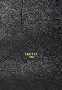 Cuir noir texturé avec un design géométrique, comportant le logo doré "Lancel Paris". Surface lisse avec un grain visible et des détails de couture.
