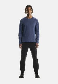 Sügavsinine, pikkade varrukatega, slim fit särk, valmistatud pehmest ja niiskust imavast kangast. Kombineeritud slim-fit mustade pükste ja mustade spordijalatsitega.