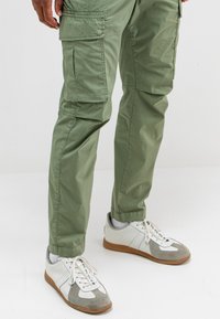 Groene cargobroek met zijzakken en een relaxed fit, gecombineerd met witte en grijze sneakers met een textuur van leer en rubberen zool.