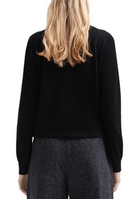 Maglione nero a maniche lunghe, design aderente, realizzato in materiale morbido, abbinato a pantaloni scuri con motivo e tasche.