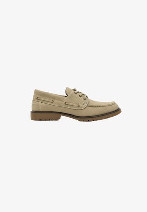 Zapato náutico de ante beige con cordones delanteros, costuras tipo moc toe y suela de goma marrón con tacos, mostrado en perfil lateral sobre fondo blanco.