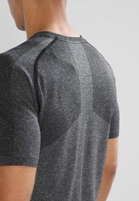 Šedé sportovní tričko s texturovaným zadním panelem, krátkými rukávy a zesílenými švy. Materiál se zdá být elastický a prodyšný.