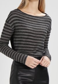 Pull à manches longues rayé gris et noir avec un large col, présentant un tissu texturé et un subtil éclat.