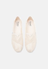 Lace slip-on shoes in cream with a floral pattern, rounded toe, and a cushioned insole. Features TOMS branding on the interior.