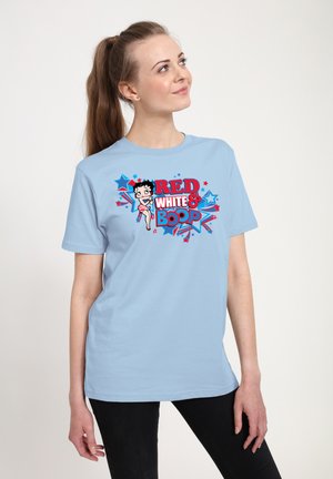 Junge Frau mit Pferdeschwanz, die ein hellblaues T-Shirt mit Betty Boop und dem Schriftzug "Red White & Boop" in Rot, Weiß und Blau trägt.
