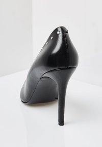 Pantof cu toc înalt, de culoare neagră, realizat din piele netedă, având tinte argintii pe partea din spate, cu vârf ascuțit și toc stiletto îngust.