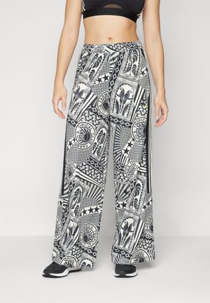 Personne portant un pantalon large noir et blanc avec des motifs géométriques et circulaires abstraits, associé à des baskets noires et un crop top noir.