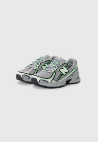 Baskets de sport en maille grises avec accents verts, dotées d'un design à lacets, d'une semelle rembourrée et d'un logo de la marque visible sur les côtés.