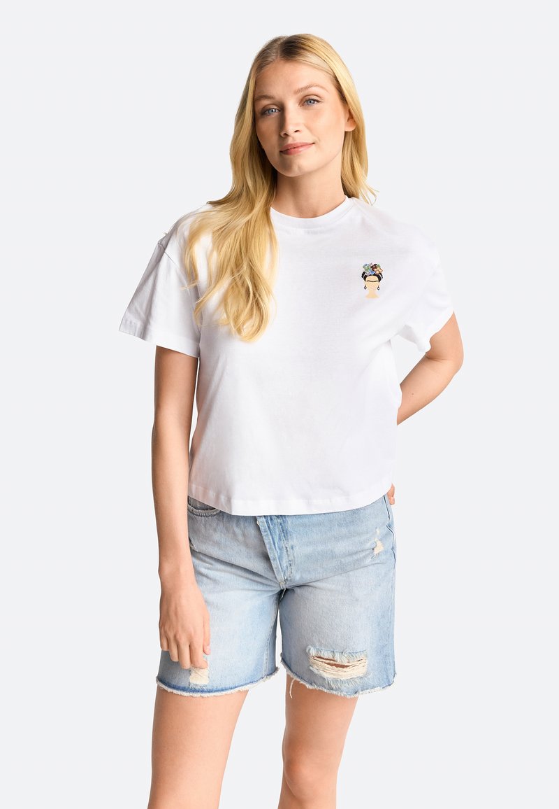 White cropped t-shirt made of soft cotton, featuring a colorful embroidered motif. Paired with light blue distressed denim shorts.