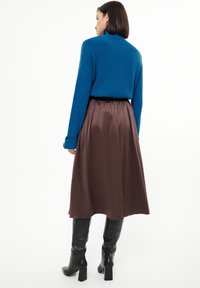 Blaues Strickpullover mit langen Ärmeln und gerippter Textur, kombiniert mit einem braunen Satrock, der bis zur Mitte der Wade reicht, ergänzt durch knielange schwarze Stiefel.
