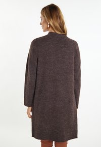 Dlouhý hnědý kardigan s měkkou, strukturovanou pleteninou, s vysokým výstřihem a mírně oversized rukávy s pokleslými rameny.
