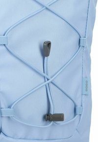 Mochila de color azul claro con una tela texturizada, diseño de cordón elástico y ajustador en color gris. Se puede ver la etiqueta lateral.