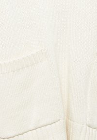 Strikket cardigan i cremefarve med ribbede kanter og to forlommer. Teksturen er blød med en løs, afslappet pasform.