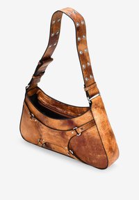 Bolso de mano de cuero marrón con forma curvada, tachuelas plateadas en la correa y cierre de cremallera. Superficie texturizada con arrugas y marcas visibles.