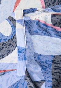 Tela multicolorida con formas abstractas en azul, gris y rosa. Textura suave con detalle de costura en contraste.