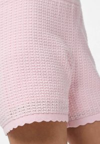 Gaiši rozā adīti šorti ar teksturētu rakstu un viļņotu apakšmalu. Izgatavoti no elpojoša materiāla komfortam.