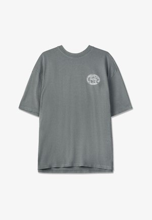Šedé bavlněné tričko s krátkými rukávy, kulatým výstřihem, volným střihem a kulatým logem vytištěným na levé části hrudi v bílé barvě.