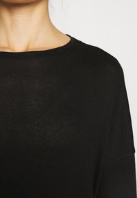 Czarny sweter dziany z okrągłym dekoltem i luźnym krojem. Tkanina ma subtelną fakturę i lekko prześwitujące miejsca.