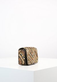 Piccolo clutch rettangolare con un motivo geometrico di perline dorate, bronzo e nere, esposto su un piedistallo bianco.