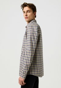 Gegolfde lichtgewicht blouse met lange mouwen in beige, marineblauw en rode tinten. Gelaagd kraag, knoopsluiting aan de voorkant en zachte katoen met een ontspannen pasvorm.