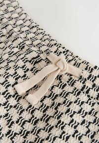 Gros plan sur un tissu texturé noir et blanc avec un cordon beige noué en haut au centre.