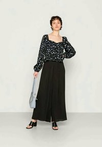 Blusa preta com bolinhas brancas e mangas bufantes, combinada com uma saia preta plissada. Os acessórios incluem uma bolsa azul clara e sandálias pretas.