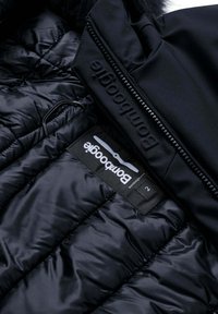 Giubbotto a vento nero con una texture lucida e design imbottito. Include una cerniera nera e un'etichetta appesa con dettagli del marchio.