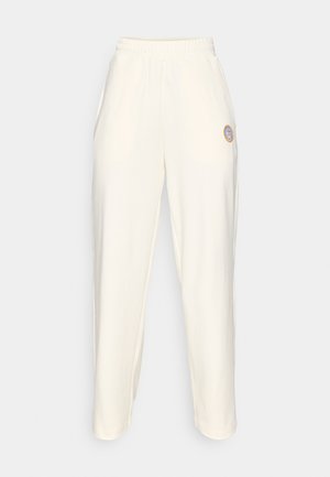 Cream-colored sweatpants with an elastic waistband, tapered legs, and a small circular logo on the left thigh. Smooth texture.