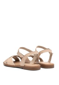 Beżowe sandały z krzyżującymi się paskami, płaską podeszwą, materiał syntetyczny i regulowanym paskiem na kostkę; gładka faktura z minimalnymi detalami.