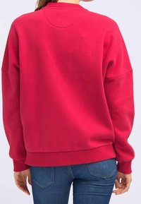 Sweatshirt en polaire rose vif, doté d'un col rond, d'épaules tombantes et de poignets et ourlet côtelés. Texture douce avec une coupe décontractée.