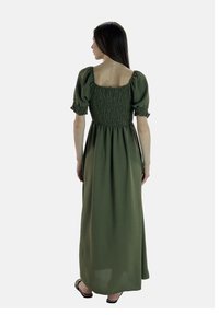 Robe longue vert olive avec un corsage smocké, des manches bouffantes et une jupe fluide. Le tissu a une texture douce avec un subtil éclat.