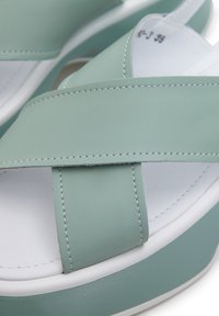 Žabky v mátově zelené barvě s návrhem křížových pásků, vyrobené z hladkého syntetického materiálu. Mají bílou podrážku se švy.