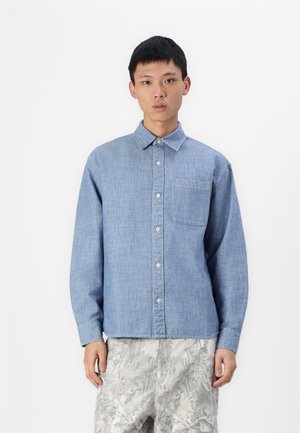 Light blue denim shirt with a collar, front pocket, and button closure. The fabric has a smooth texture and long sleeves.