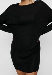 Vestido negro de punto con un escote amplio y suelto, mangas largas y una parte inferior ajustada. La tela tiene un ligero brillo y una textura suave.