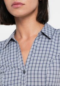 Πουκάμισο σε ναυτικό μπλε και λευκό καρό με κουμπιά και γιακά. Διαθέτει ένα μόνο μαύρο κουμπί στον γιακά και απαλό υλικό.