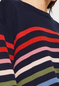 Gebreide trui met horizontale strepen in rood, roze, crème, groen en blauw op een marineblauwe achtergrond; ronde halslijn en gestructureerde stof.